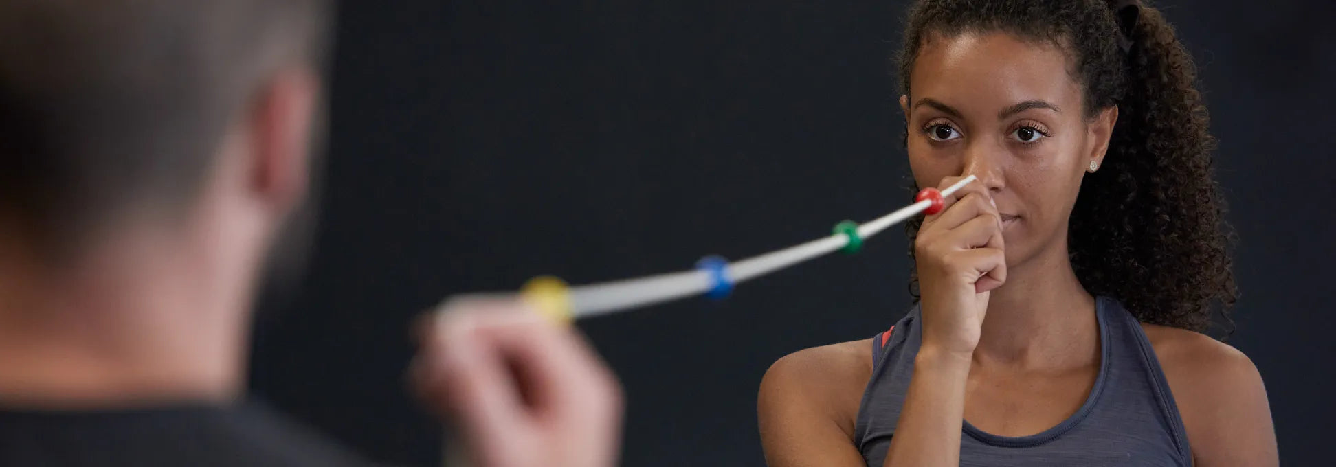 Eine Frau hält sich ein Ende eines Brock Strings an die Nasenspitze, während ein Mann das andere Ende mit der rechten Hand festhält.