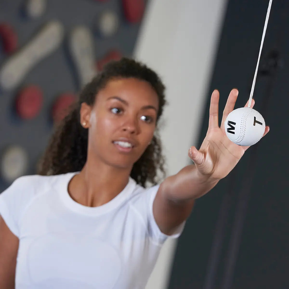 Eine Frau in weißem T-Shirt greift mit der linken Hand nach einem ARTZT neuro Marsden Ball, der vor ihr von der Decke hängt.