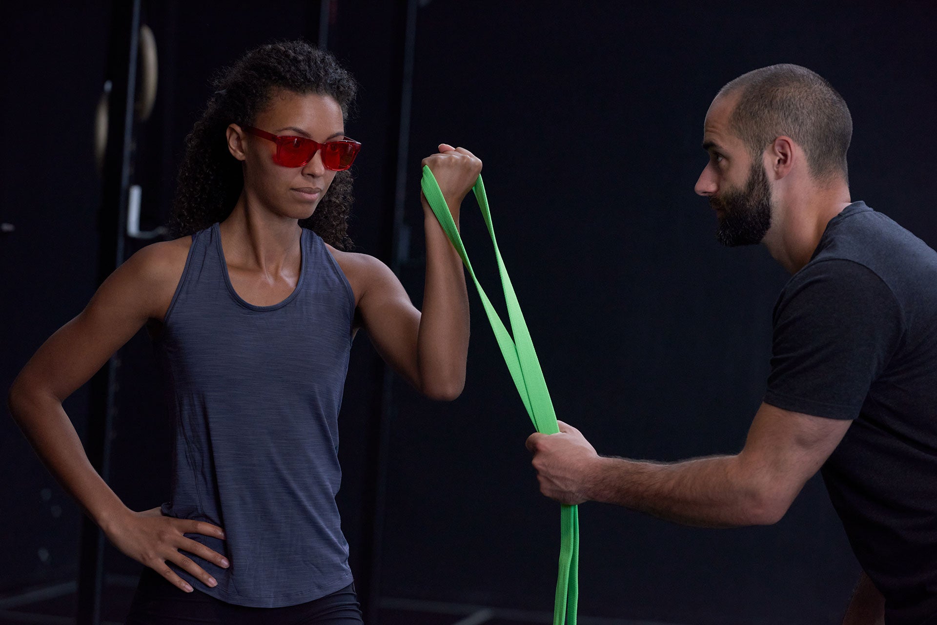 Frau trägt eine rote ARTZT neuro Farbbrille und trainiert mithilfe eines Trainers mit einem Fitnessband.