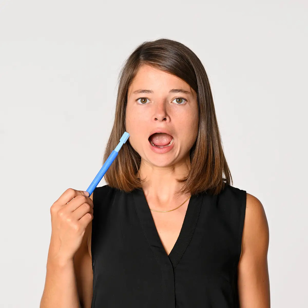 Eine Frau vor hellgrauem Hintergrund öffnet den Mund und hält einen blauen Z-Vibe Vibrationsstift an ihre rechte Wange.