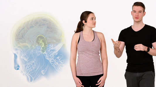 Neuroathletiktrainer Kevin Grafen steht neben einer Frau, die den ARTZT neuro SoundVibe Knochenschall Kopfhörer trägt.