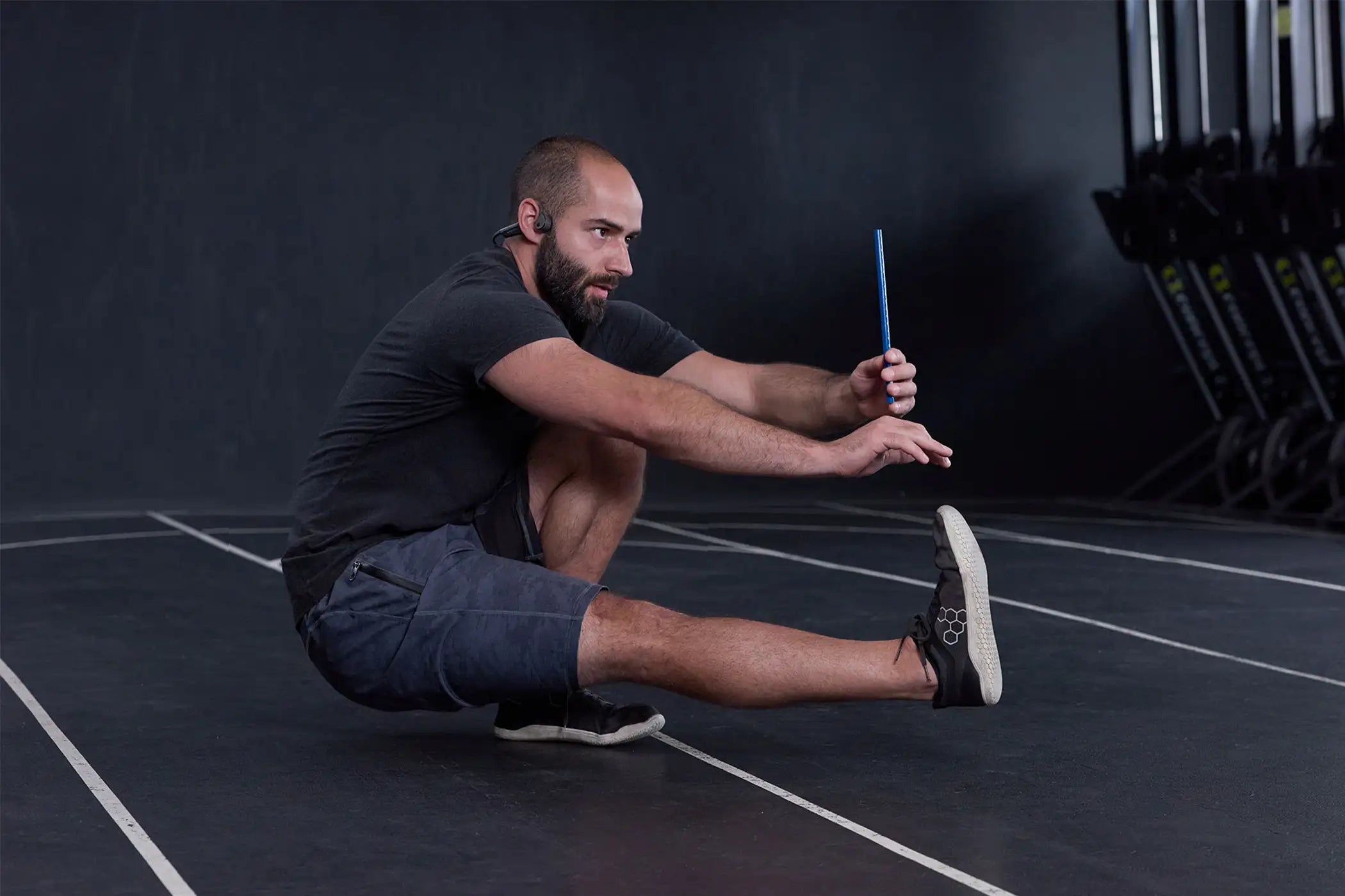 Mann bei einer Balance Übung, bei der er auf dem linken Bein hockt und das rechte Bein nach vorne ausstreckt; vor sich hält er ausgestreckt einen ARTZT neuro Vision Stick in der linken Hand.