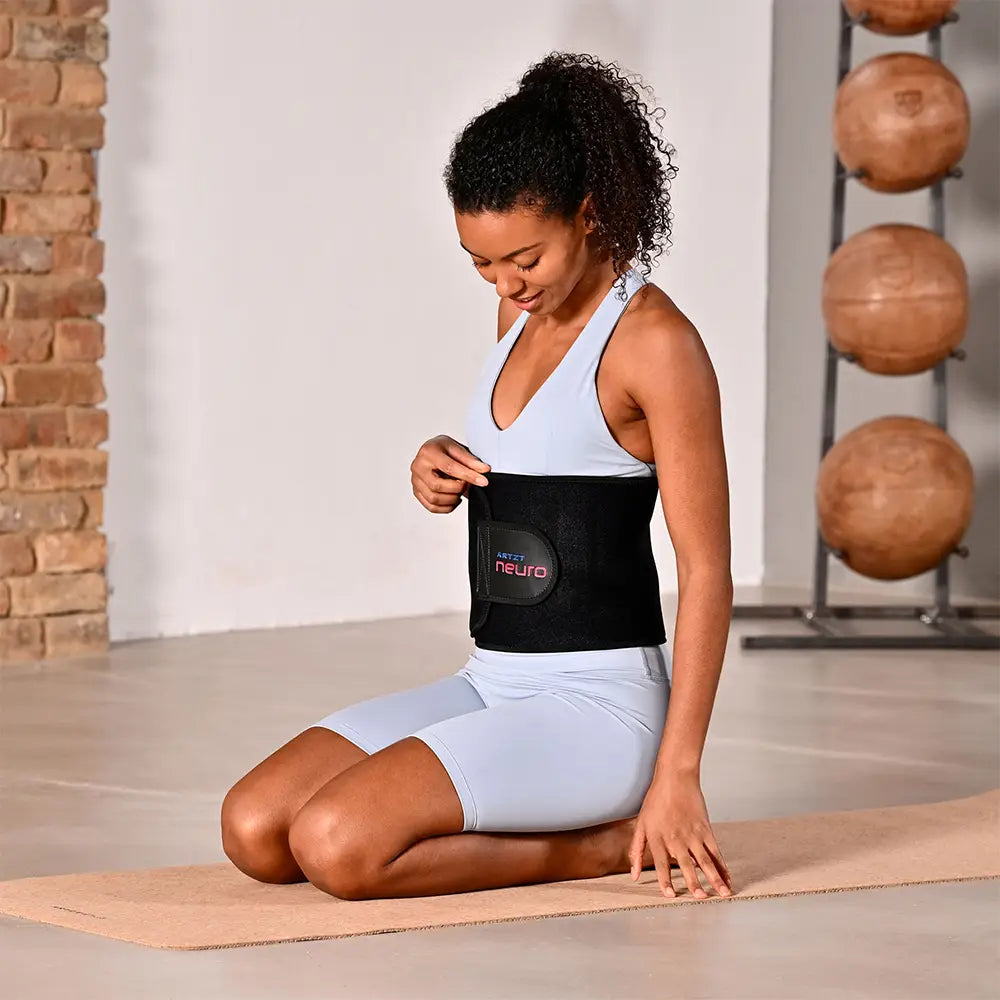 Eine frau hockt auf den Knien auf einer Yogamatte und trägt um die Taille einen ARTZT neuro Atemgürtel.