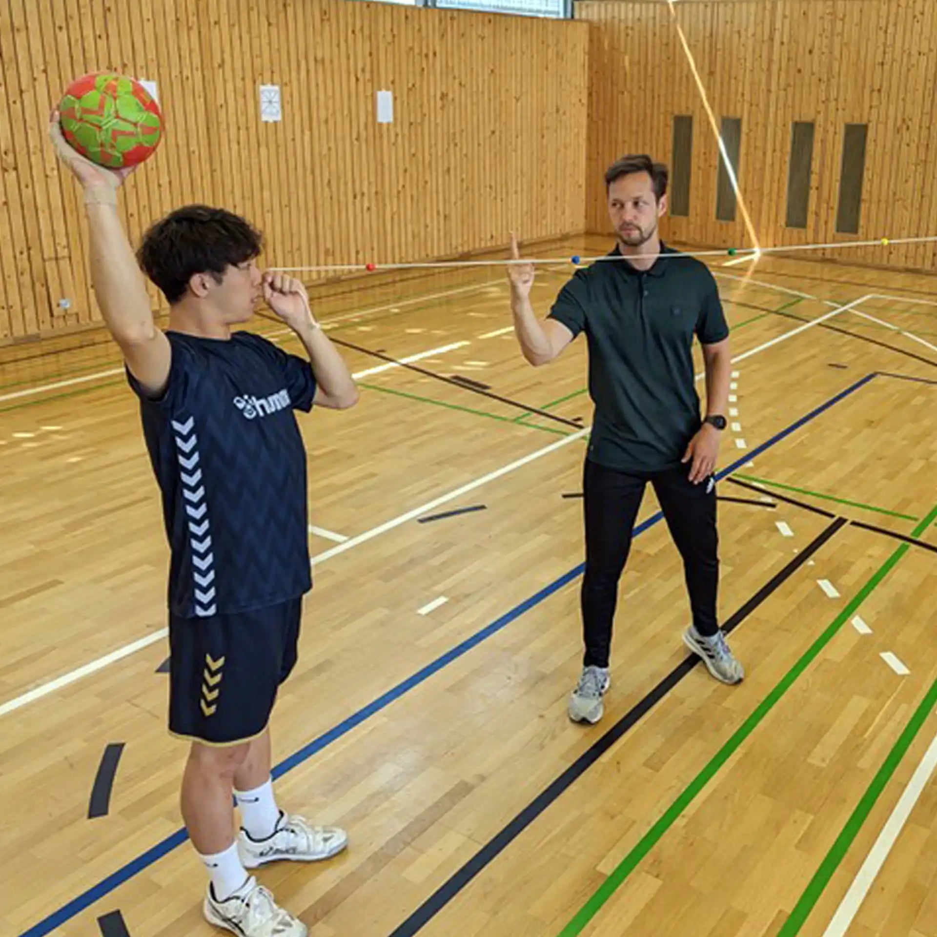 Ein Mann mit einem Ball in der rechten Hand hält mit der linken Hand eine Brock Schnur an seine Nasenspitze.