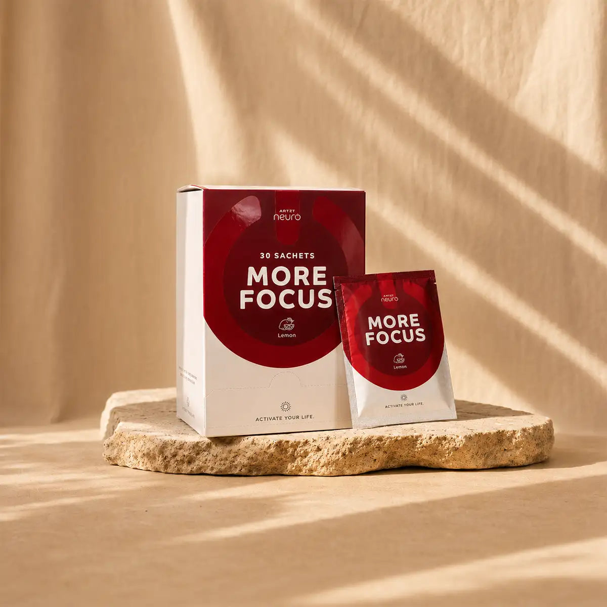 More Focus Nootropikum von ARTZT neuro – Verpackung mit 30 Sachets und einzelnes Sachet Lemon auf Steinsockel vor warmem Sandbeige-Hintergrund.