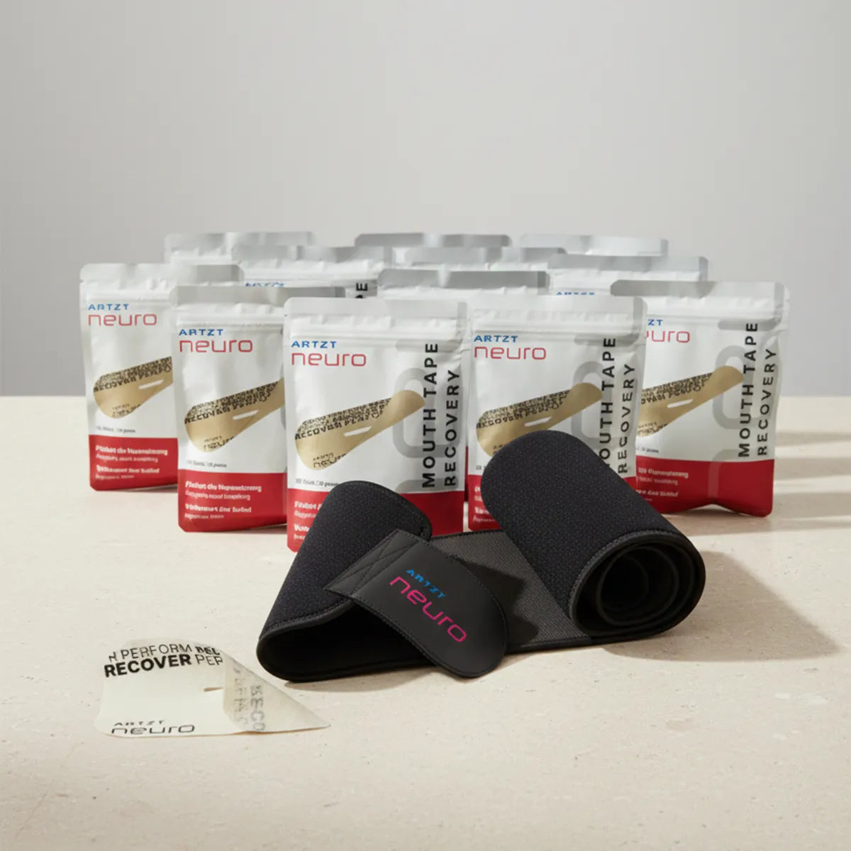 Produktaufnahme des ARTZT neuro Awareness Breathing Set mit zwölf Packungen Mouth Tape Recovery, einem ausgerollten schwarzen Atemgürtel mit ARTZT neuro Logo sowie einem einzelnen Mouth Tape auf hellem Untergrund vor neutralem Hintergrund. SET-1023 #mengenrabatt_12 monate