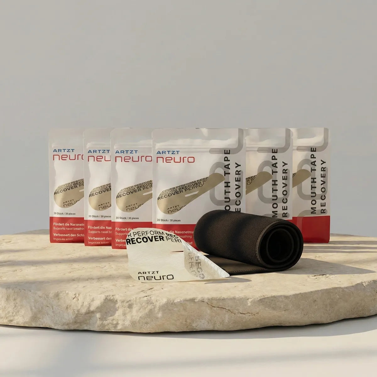 Produktaufnahme des ARTZT neuro Awareness Breathing Set mit sechs Packungen Mouth Tape Recovery, einem aufgerollten schwarzen Atemgürtel sowie einem einzelnen Mouth Tape, arrangiert auf einer naturbelassenen Steinplatte vor hellem Hintergrund. SET-1022 #mengenrabatt_6 monate