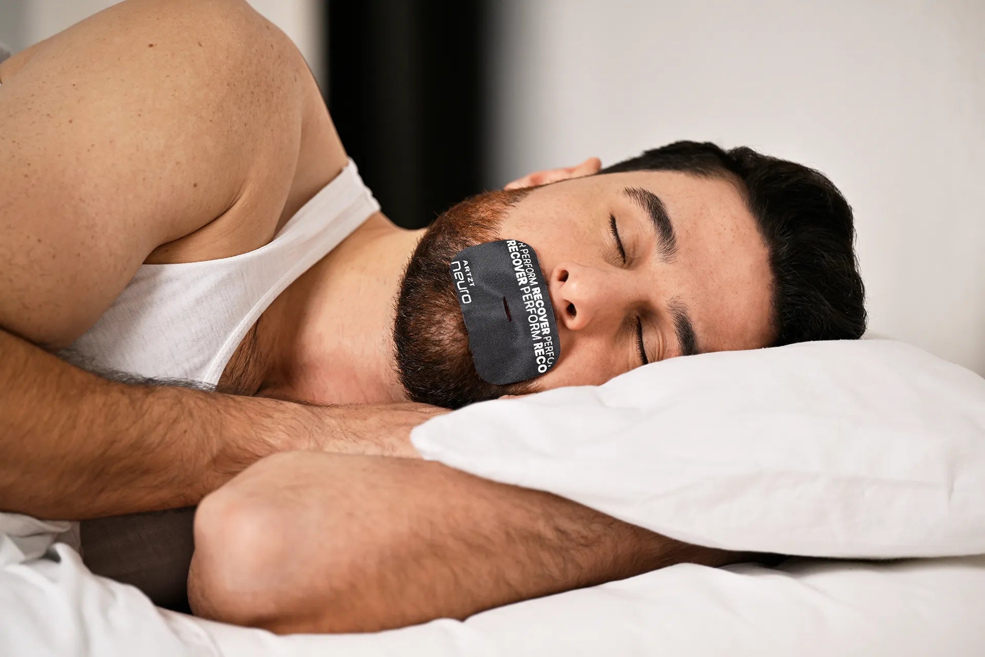 Mann liegt auf der Seite mit geschlossenen Augen und trägt auf dem Mund ein schwarzes ARTZT neuro Mouth Tape Recovery