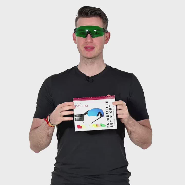 Ein Mann vor weißem Hintergrund hält die Verpackung des ARTZT neuro Farbbrillen Sets in beiden Händen und trägt eine rote Farbbrille.