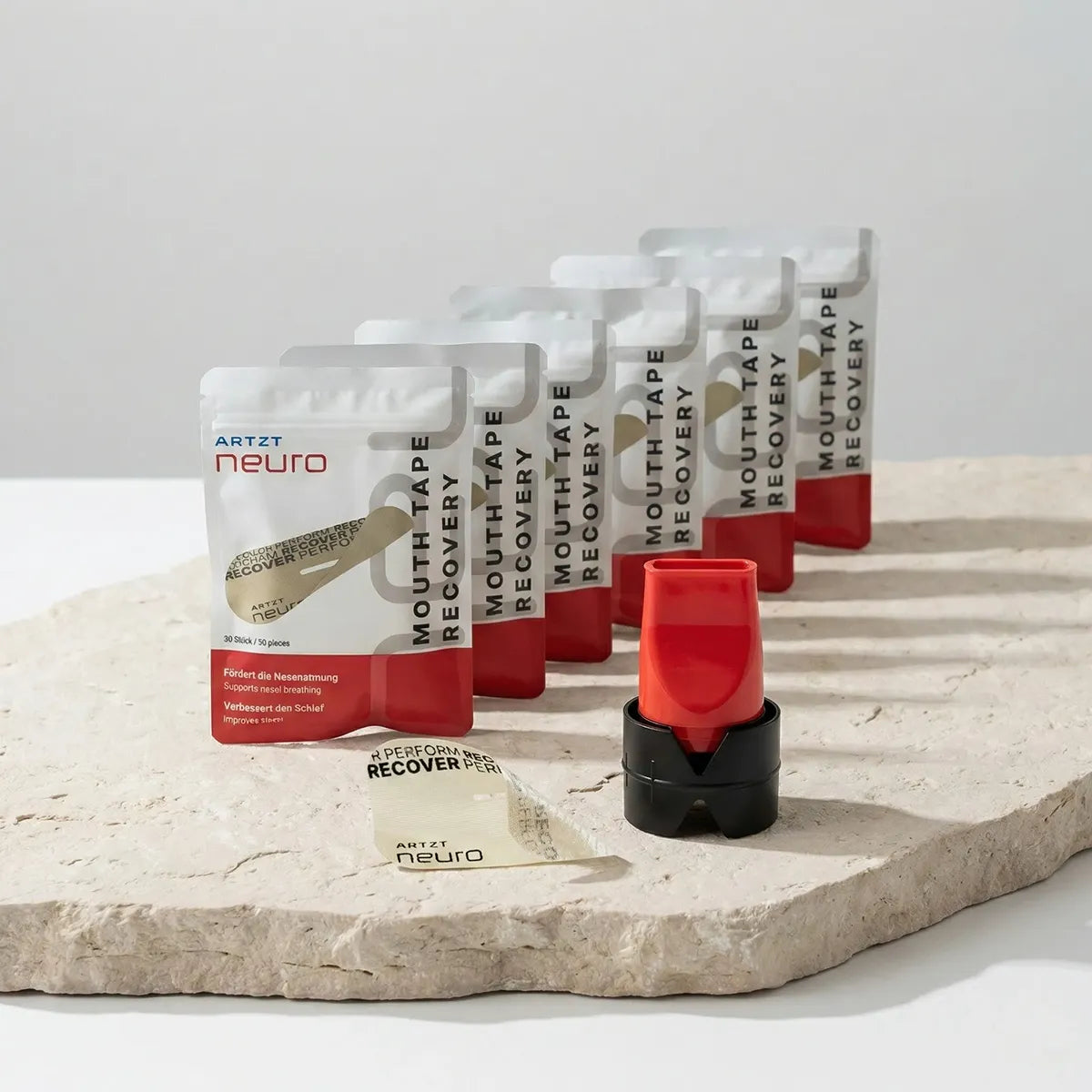 Produktaufnahme des ARTZT neuro Recovery Breathing Set mit mehreren Packungen Mouth Tape Recovery, einem roten Atemtrainer mit schwarzem Standfuß sowie einem einzelnen Mouth Tape auf einer naturbelassenen Steinplatte vor hellem Hintergrund. SET-1020 #mengenrabatt_6 monate